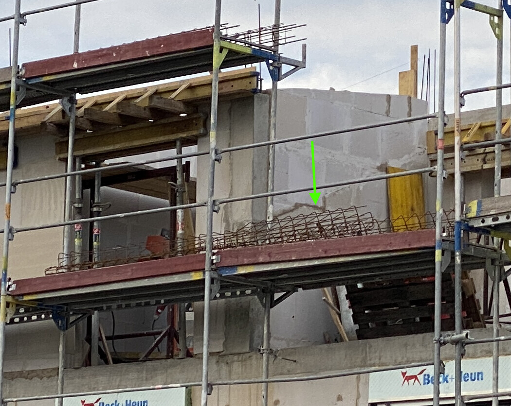 Baustelle mit Gerüst und Betonwand; Bewehrungsstahl liegt auf dem Rand der Betonplatte.