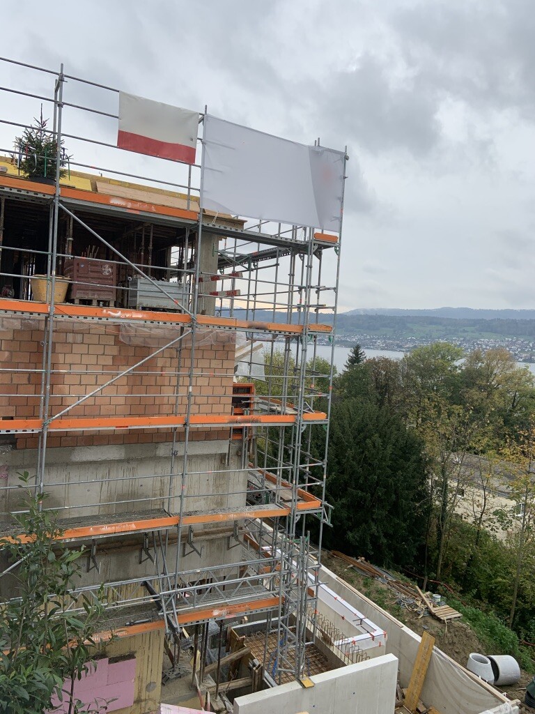 Baustelle mit Gerüst um einen Ziegelbau; Blick auf See und umliegende Hügel.