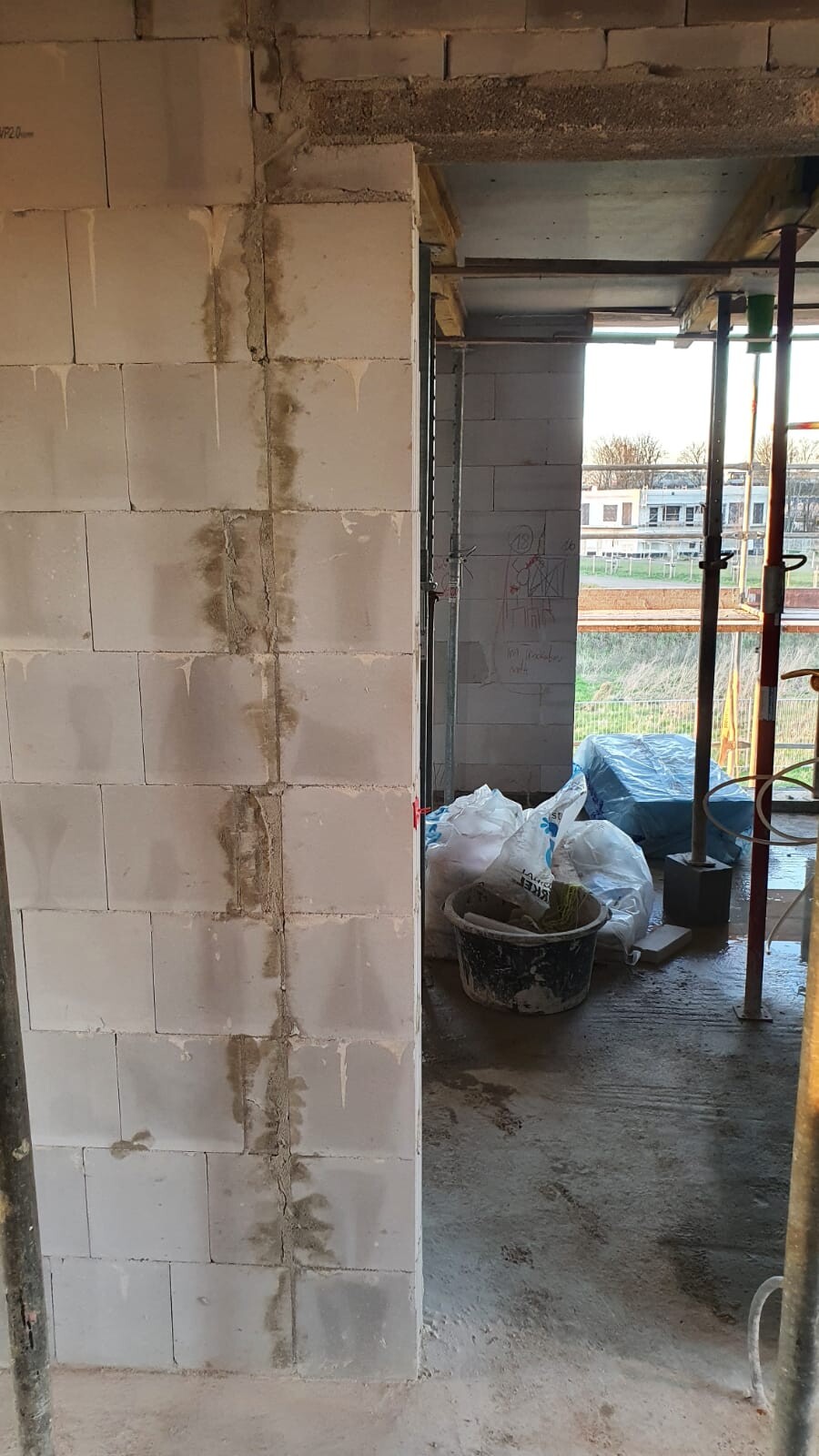 Innenraum einer Baustelle mit weißen Betonblöcken, Eimer und Säcken; Blick nach draußen.