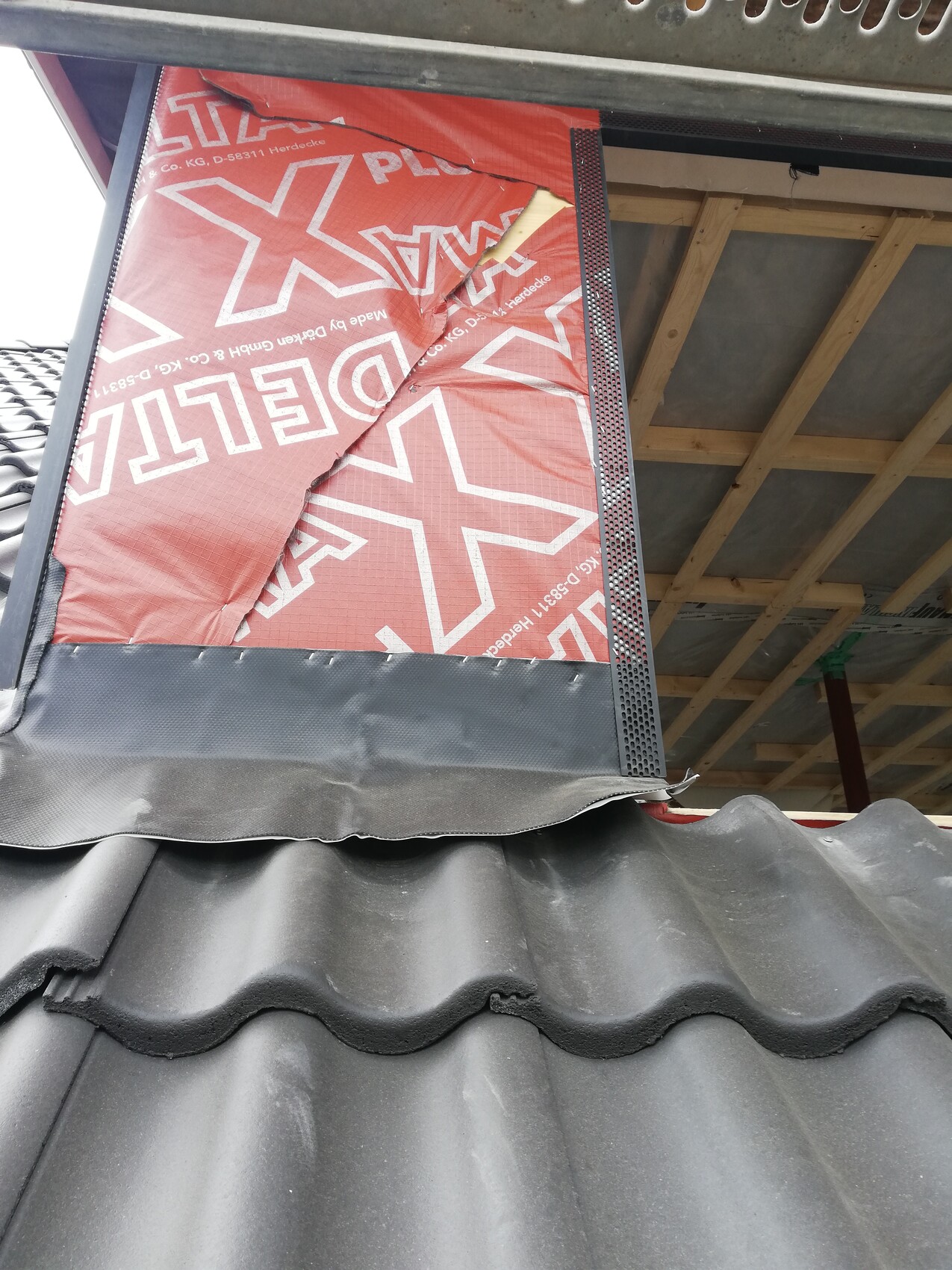 Dachkonstruktion mit roter Baufolie, Holzrahmen und dunklen gewellten Dachziegeln.
