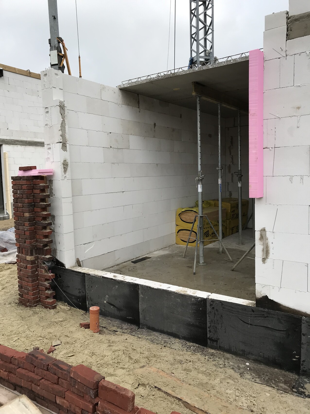 Baustelle im Rohbau mit weißen Betonblockwänden, pinkem Dämmstoffstreifen und Gerüststützen