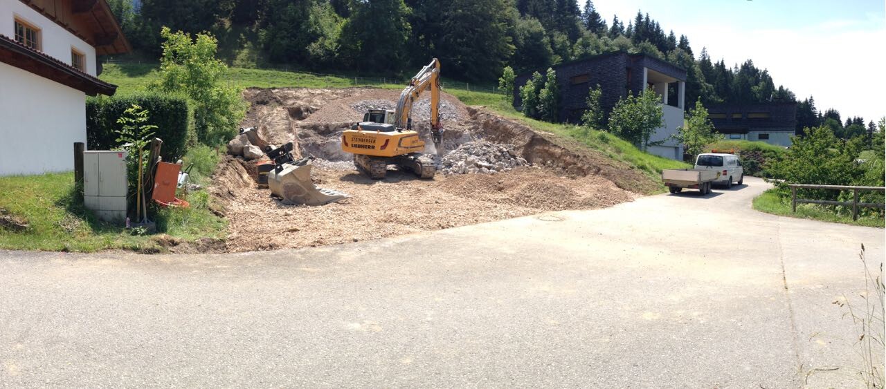 Baustelle mit Bagger, Erdhaufen und angrenzenden Häusern auf einer Landstraße