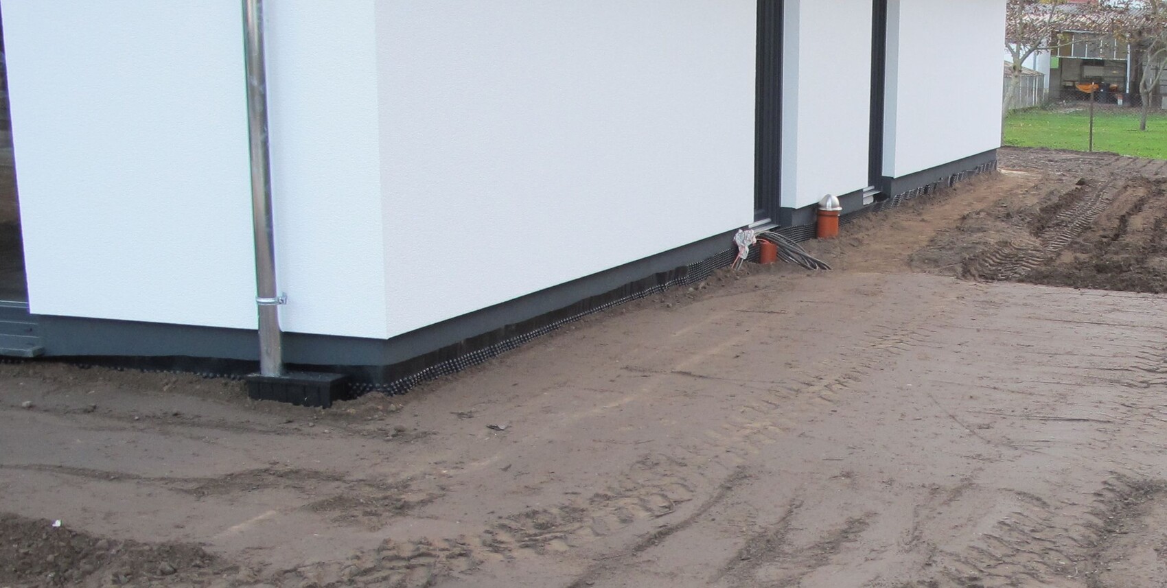 Außenansicht eines Neubaus: weiße Fassade, Erdarbeiten am Fundament und Kabelreste.
