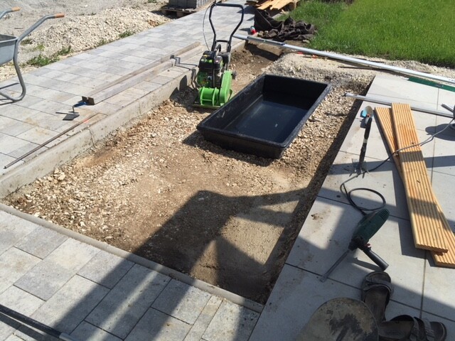 Baustelle mit Graben, Pflastersteinen, Werkzeugen und Baukonstruktion im Gartenbereich