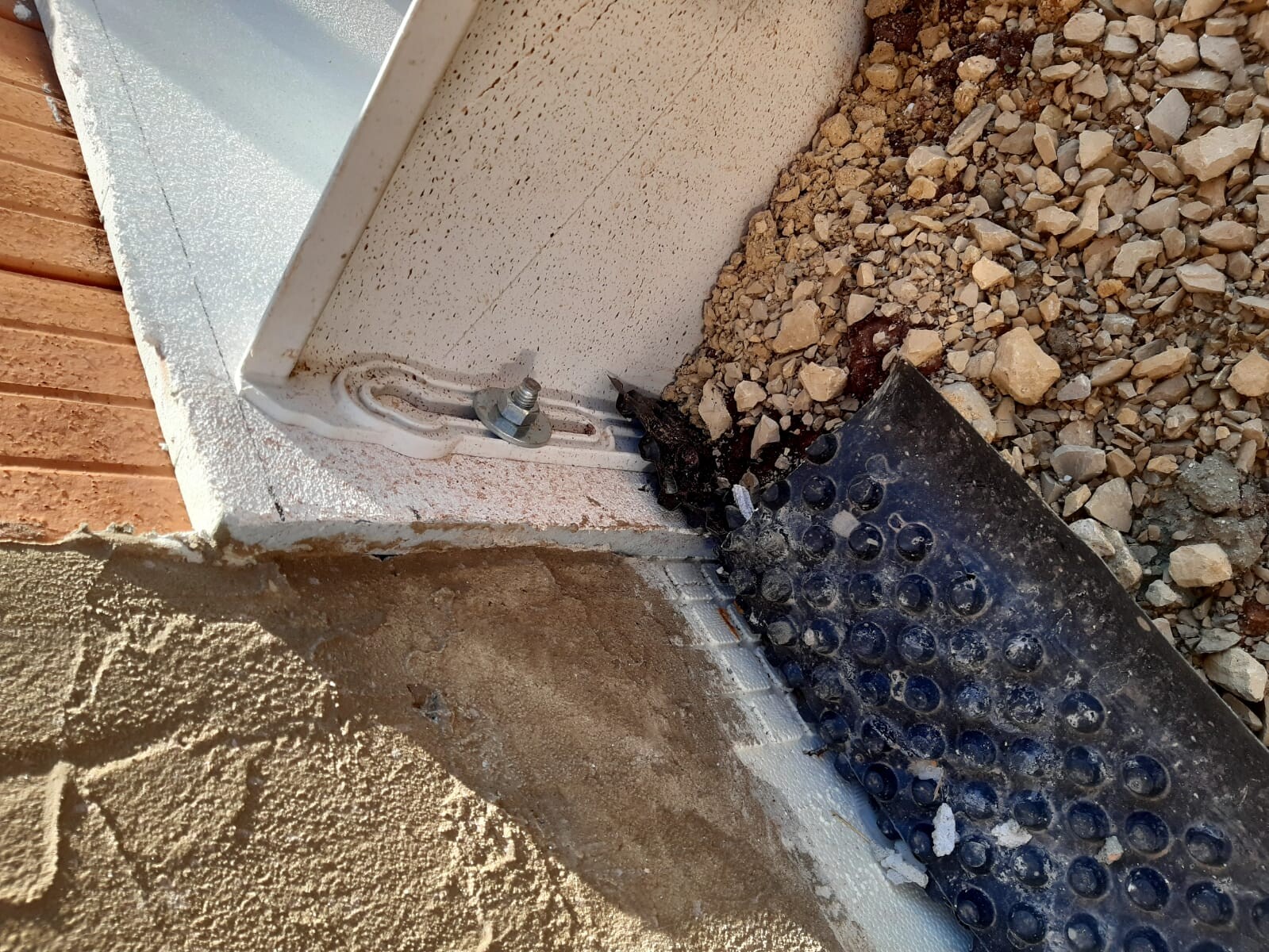 Baustelle am Fundamentrand mit Ankerbolzen, Kies und Erdmaterial neben der Außenwand.