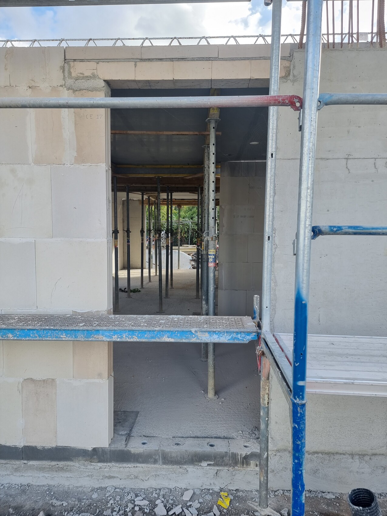 Baustelle: Innenansicht eines Gebäudes mit Gerüststützen, Durchgang und Betonwänden.