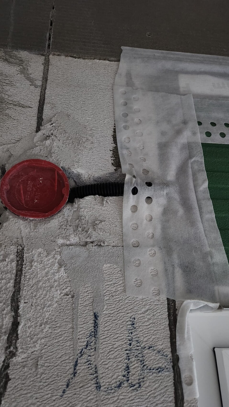 Runde rote Abdeckung mit schwarzem Kabel auf staubigem Betonboden neben perforierter Schutzfolie.