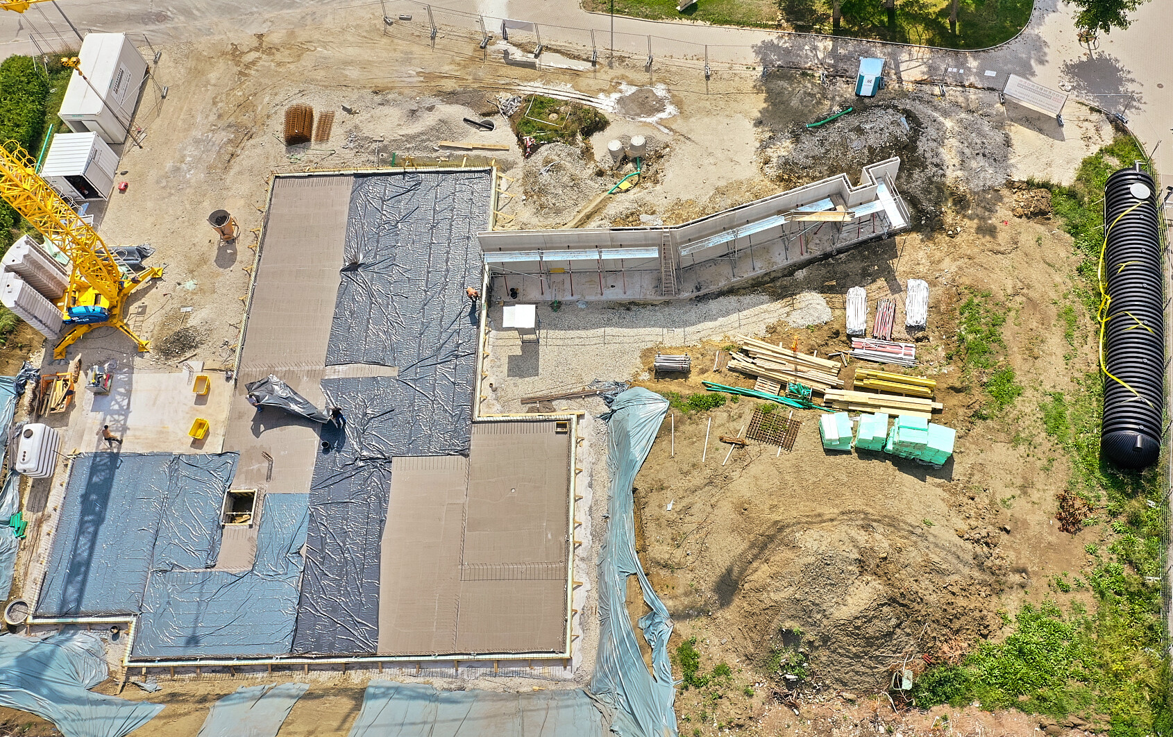 Vogelperspektive auf eine Baustelle: Gelber Kran, Betonfundament und Materialstapel.