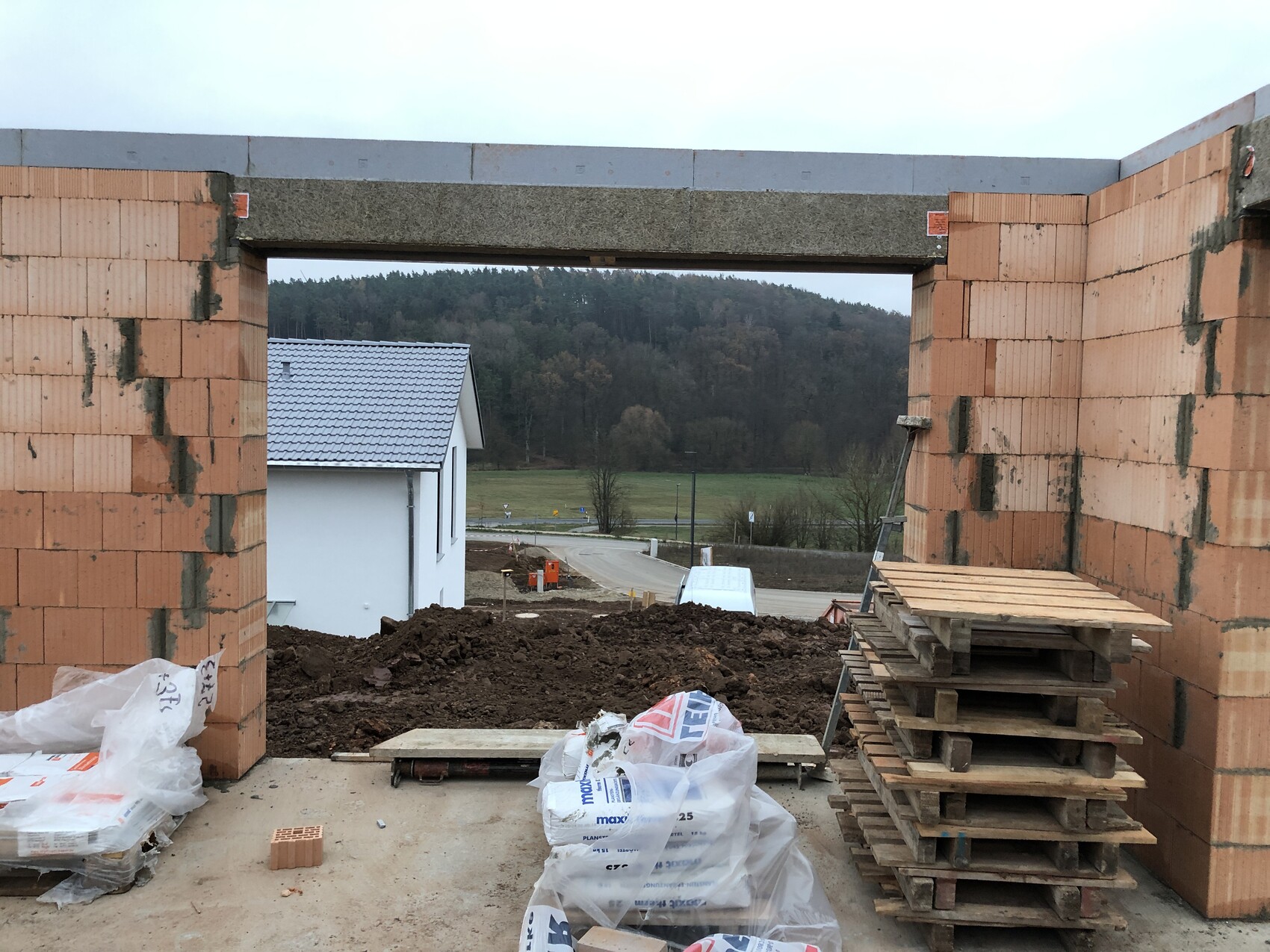 Unfertige Baustelle: Ziegelwände mit großem Durchbruch, Blick auf Hof, Wald und Paletten