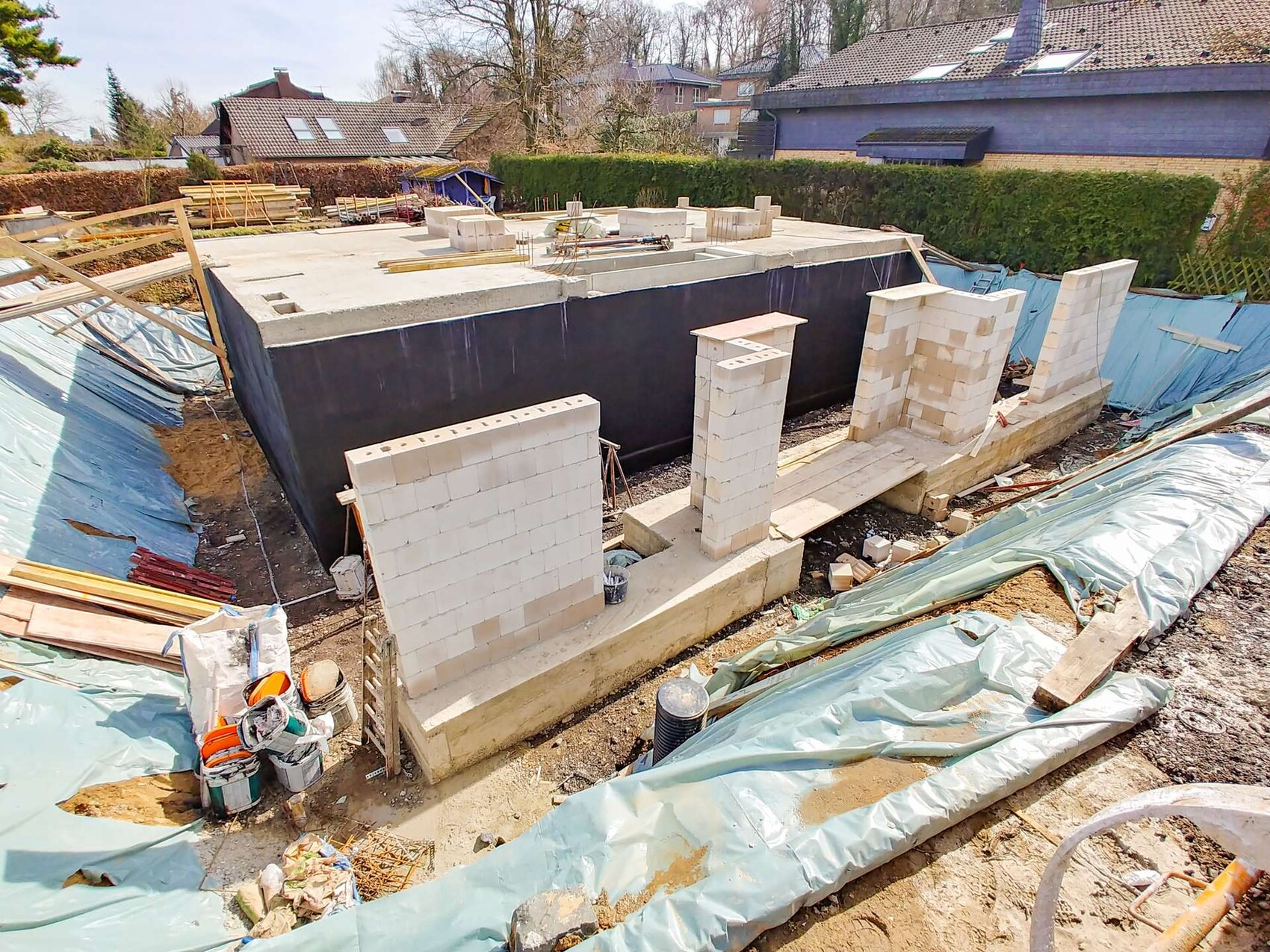 Baustelle mit Fundamentmauern aus Betonblöcken, Bauholz und Planen rundherum