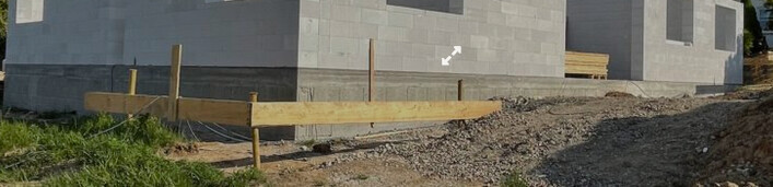 Baustelle: Betonwand aus Blöcken, Holzformen als Absperrung, Kiesboden.