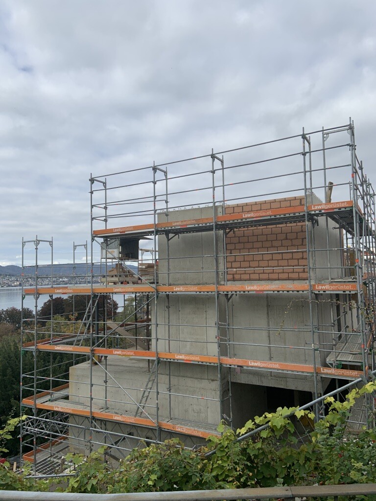 Baustelle: Gerüst um Rohbau aus Beton und Ziegel, Blick auf Landschaft im Hintergrund.