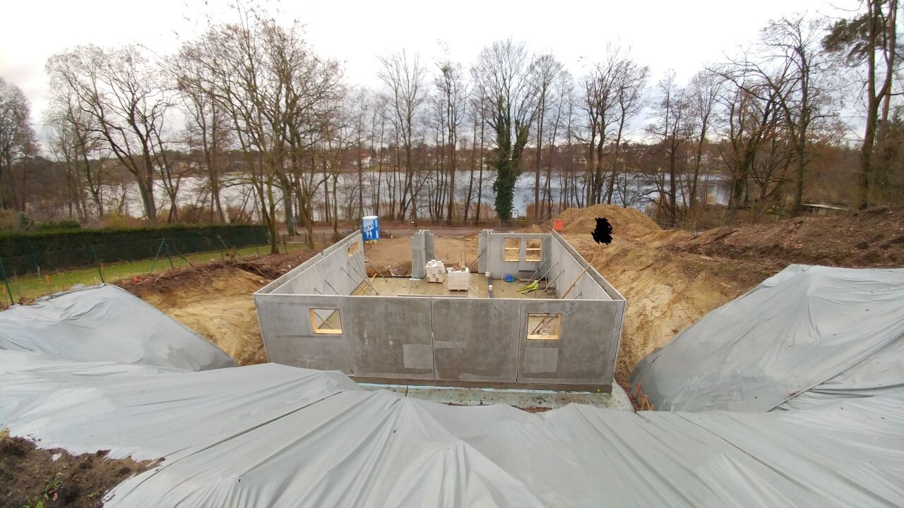 Betonfundament mit Fensteröffnungen; Erdwall, Planen und Bauarbeiten am Seeufer.