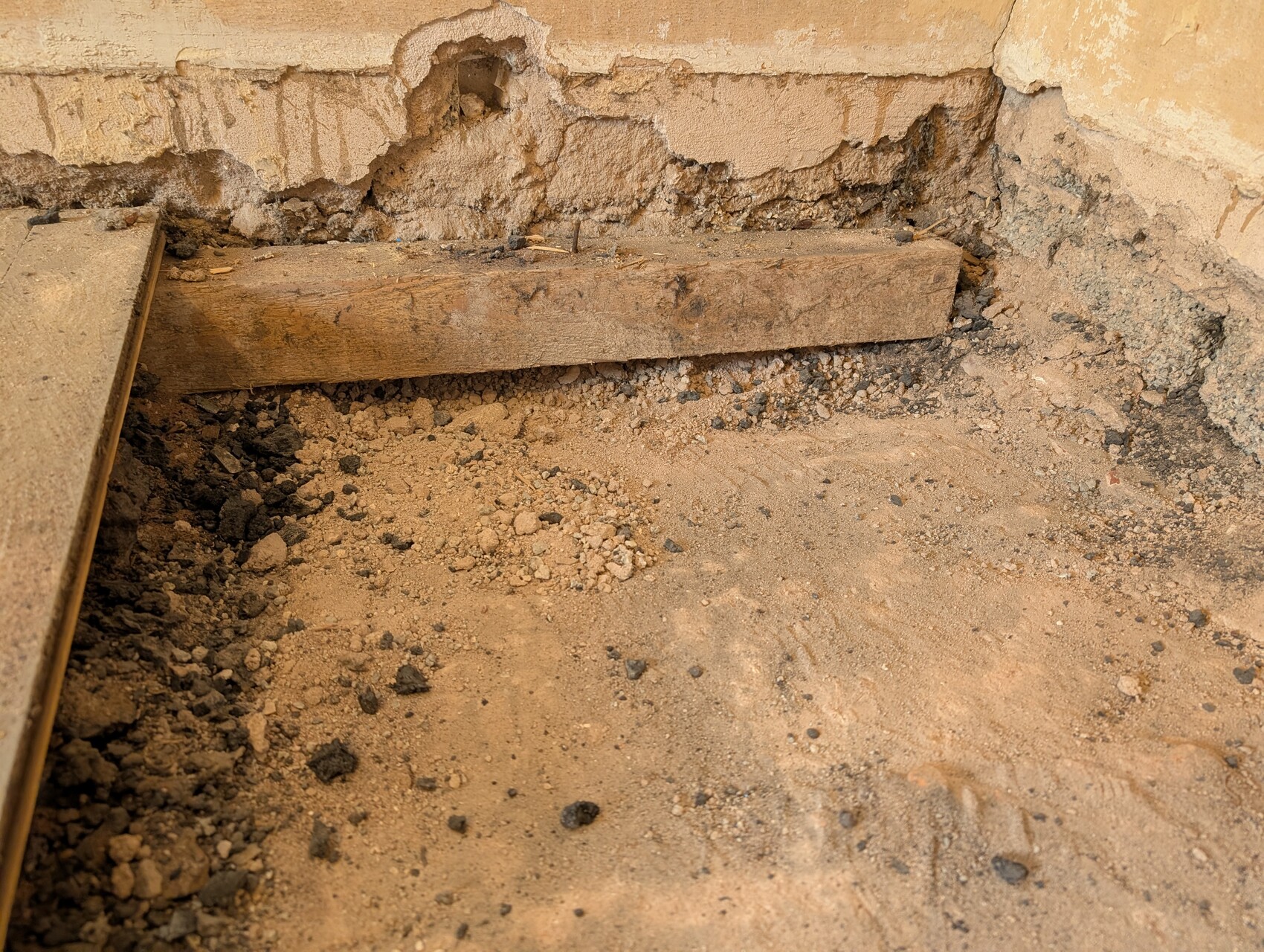 Baustellenszene: Erdreich, Holzbalken und eine grobe Fundamentwand in einer Baugrube.