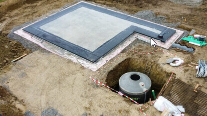 Fundament und Bodenplatte eines Baugrundstücks mit Baugrube und Baumaschinen