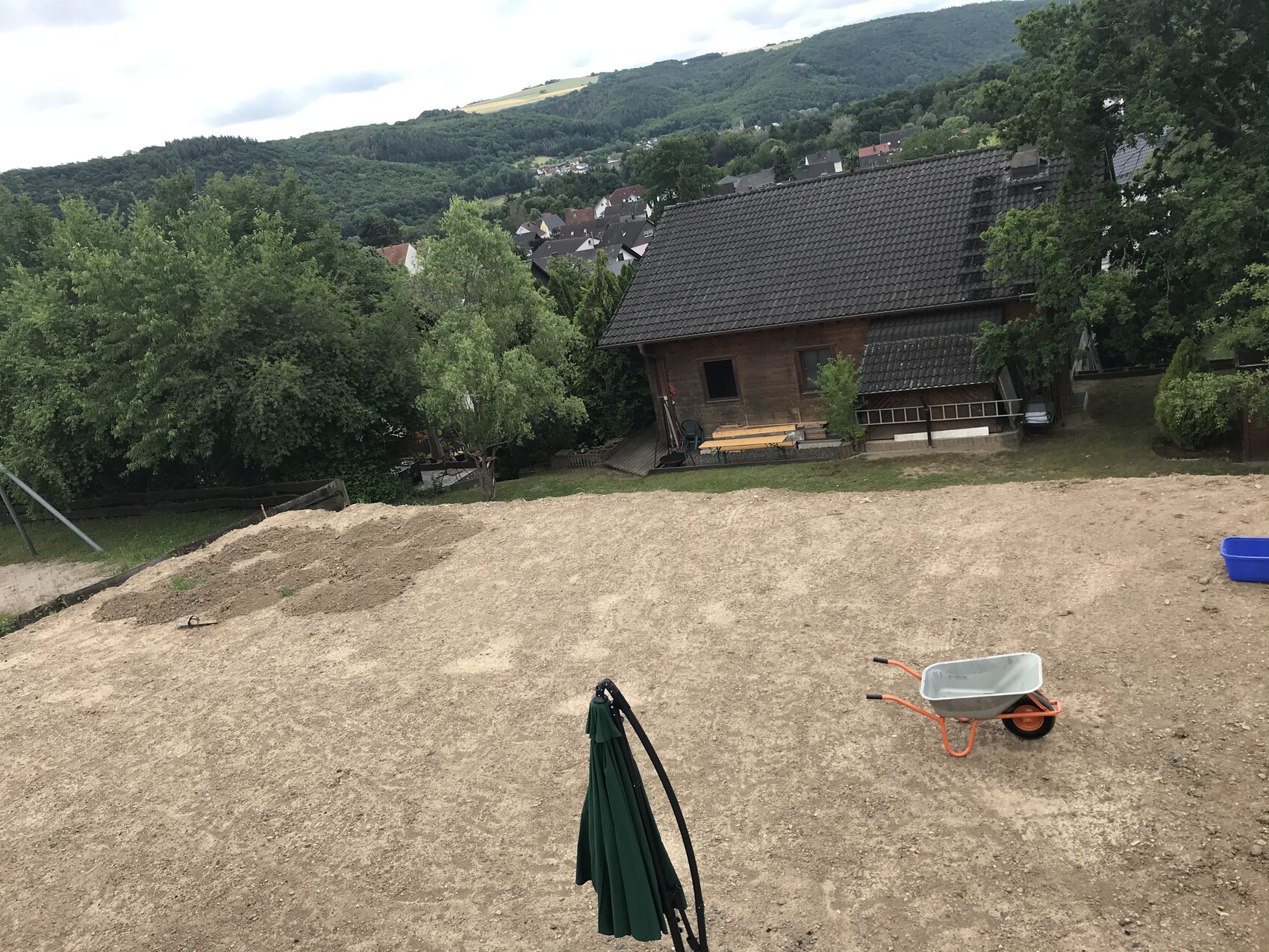 Baustellenfläche mit Erde, Schubkarren und Holzhaus im Garten auf Hanglage