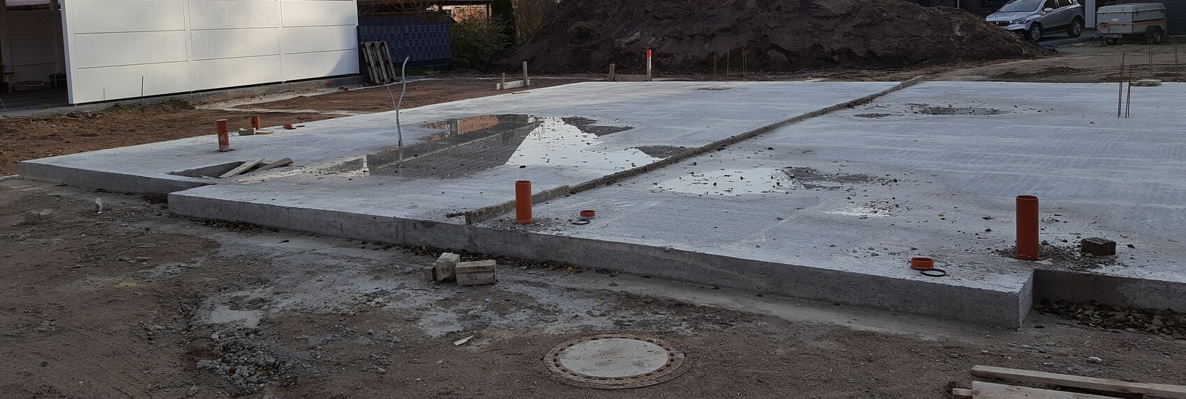 Große Betonfundamentplatte auf Baustelle mit Rohren und Erdarbeiten