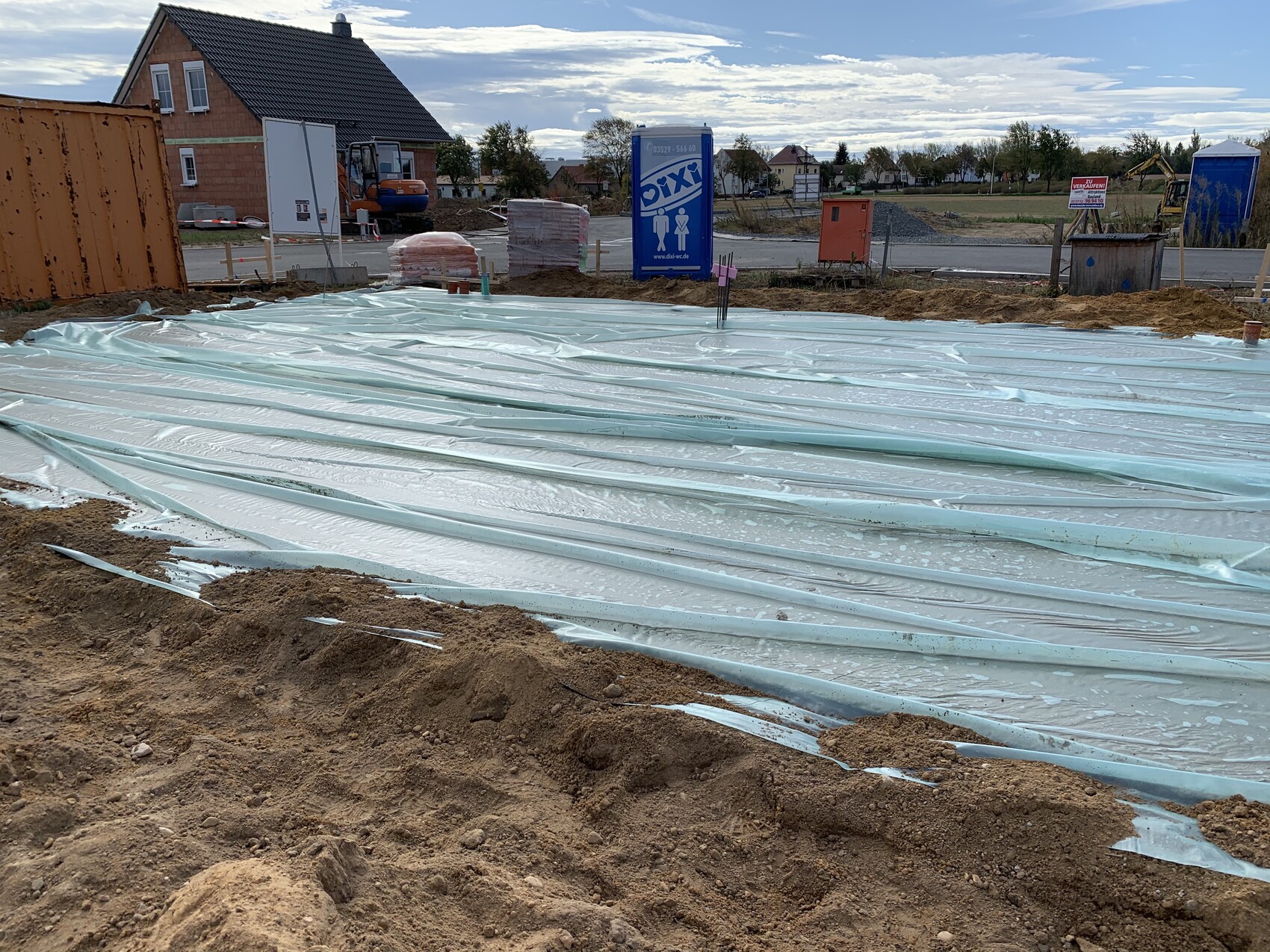 Baustelle mit blauer Bodenschutzfolie, Porta-Potty und Baugeräte im Hintergrund