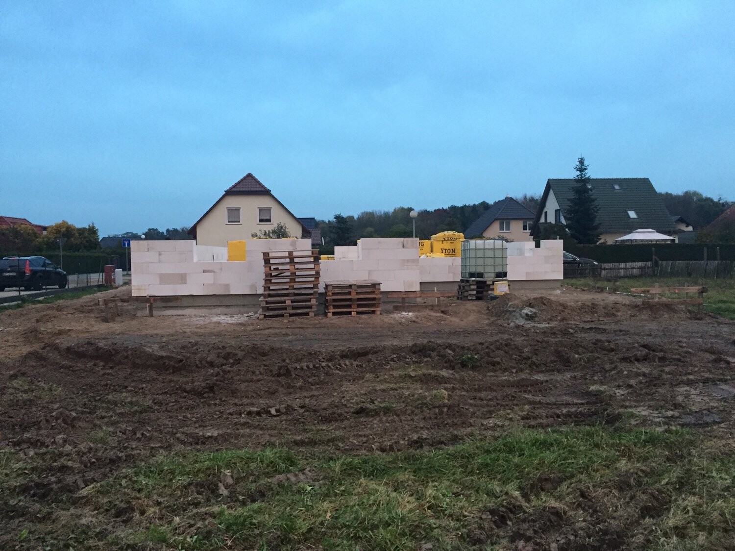 Baustelle mit gestapelten weißen Porenbetonsteinen, Paletten und Bauzubehör, Häuser im Hintergrund