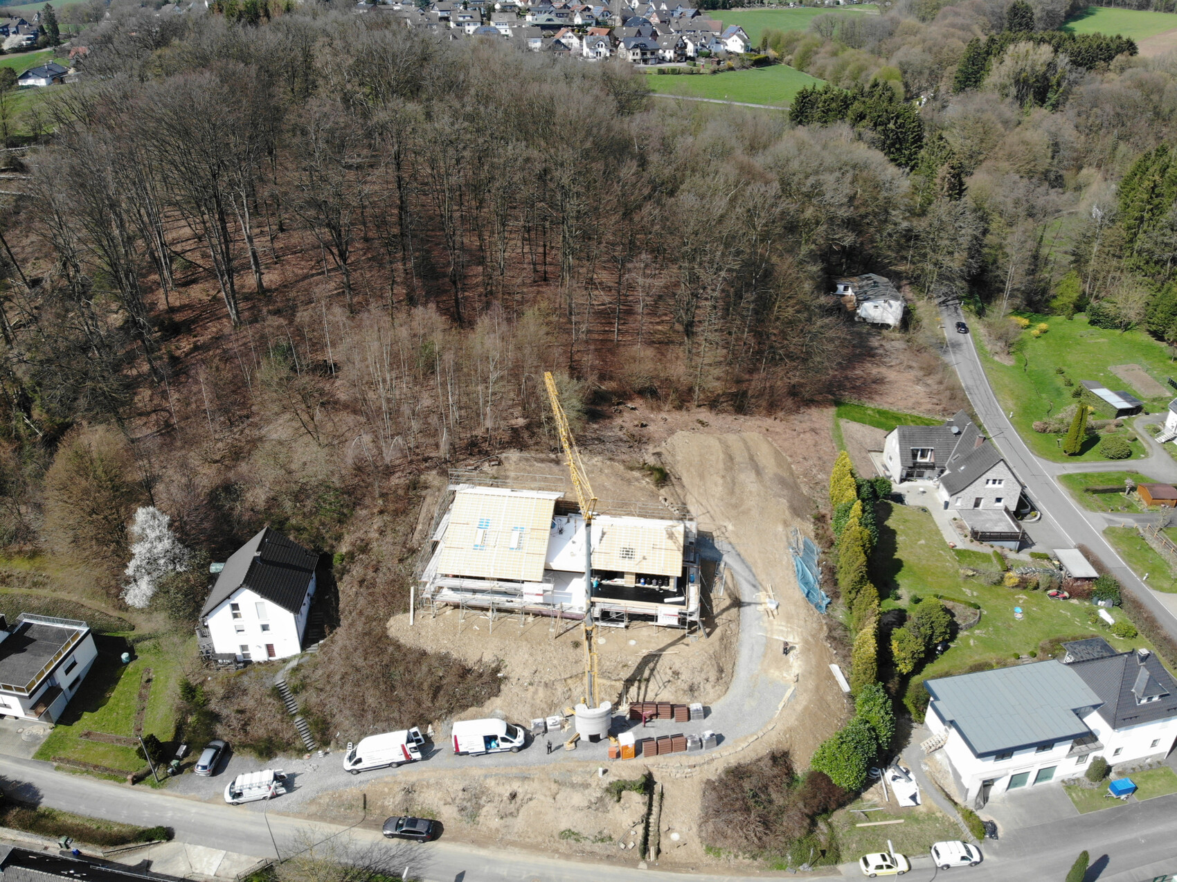 Baustelle mit Baukran neben halbfertigem Haus, umgeben von Wald und Wohngebieten