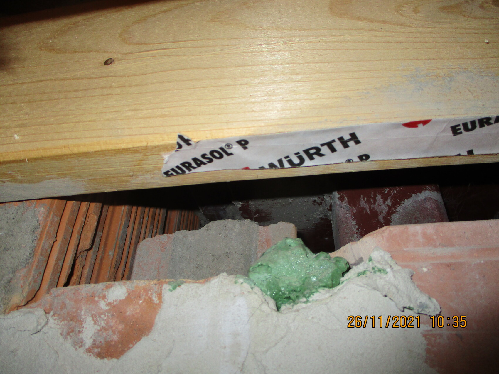 Baustelle: Holzbalken über Ziegel- und Mörtelreste, grünlicher Montageschaum und Klebeband.