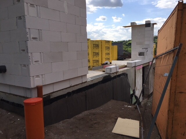 Baustelle mit weißen Betonblöcken, gelber YTONG-Blockstapel im Hintergrund, Bauzaun rechts.