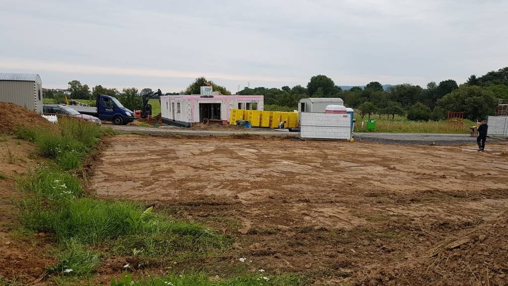 Baustelle mit Erdarbeiten, Fundament, Baucontainer und Baumaschinen auf freiem Grundstück