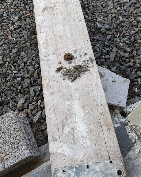 Holzbrett auf Kiesboden mit Schmutzklumpen und Baustoffresten drumherum
