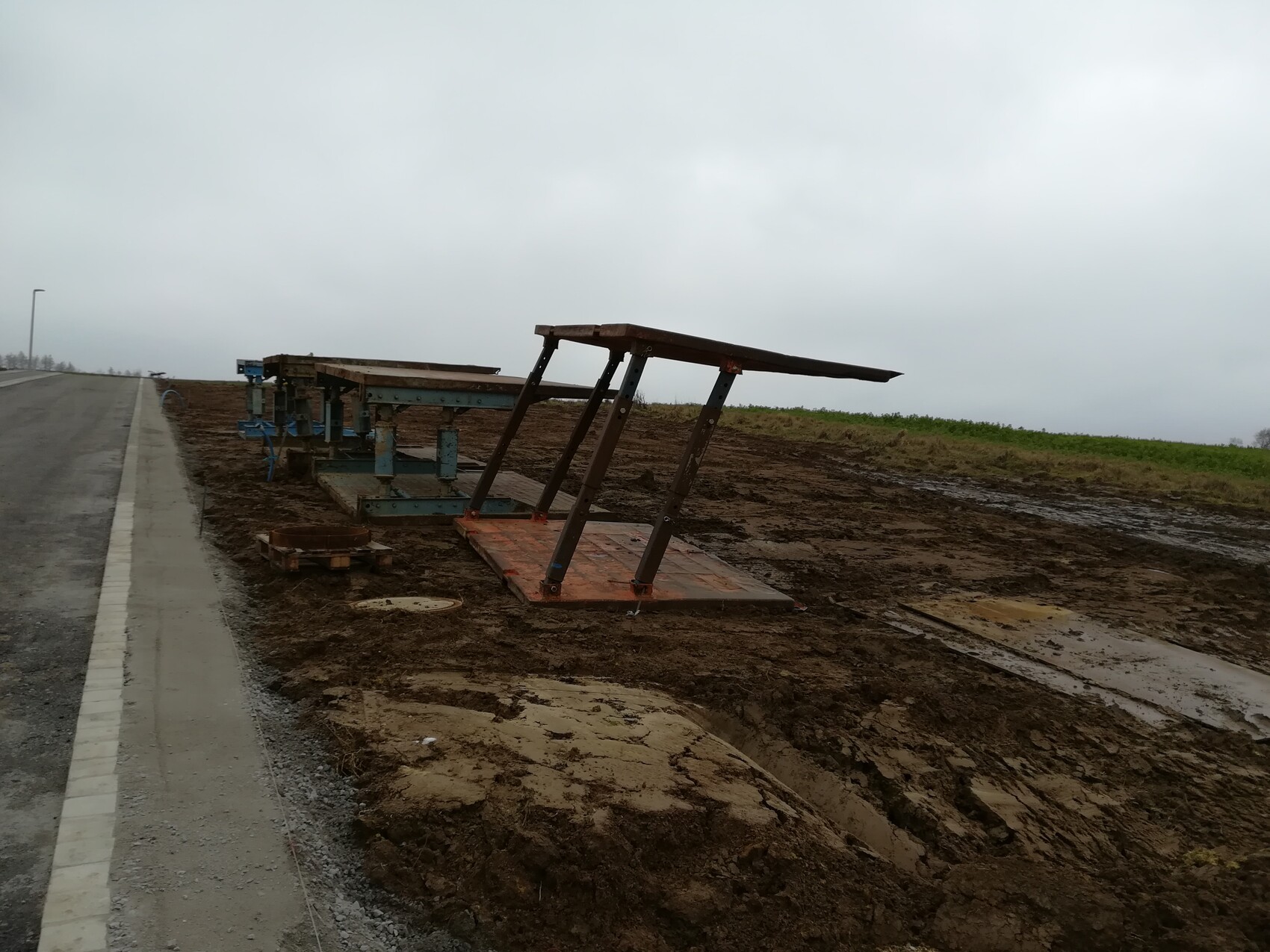 Am Straßenrand rostiges Metallgestell, schräg stehende Platte auf schlammigem Boden.