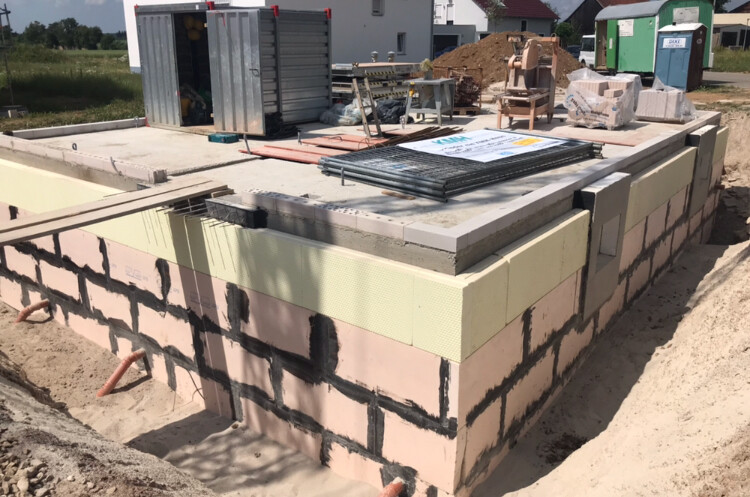 Fundamentmauer aus Blöcken, Dämmung sichtbar, Baucontainer auf Baustelle