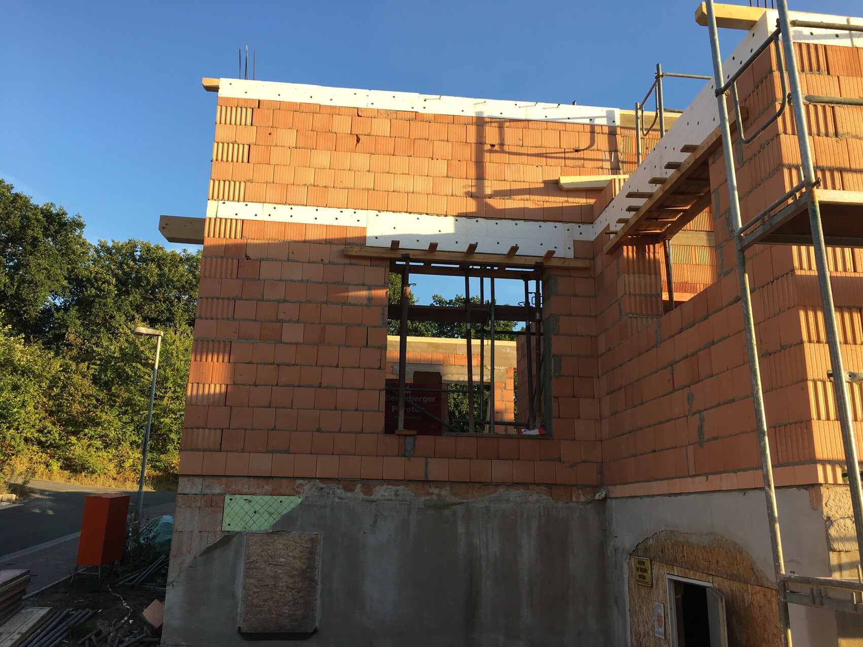 Rohbau aus Ziegeln mit Fensteröffnung, Gerüst rechts und blauem Himmel.