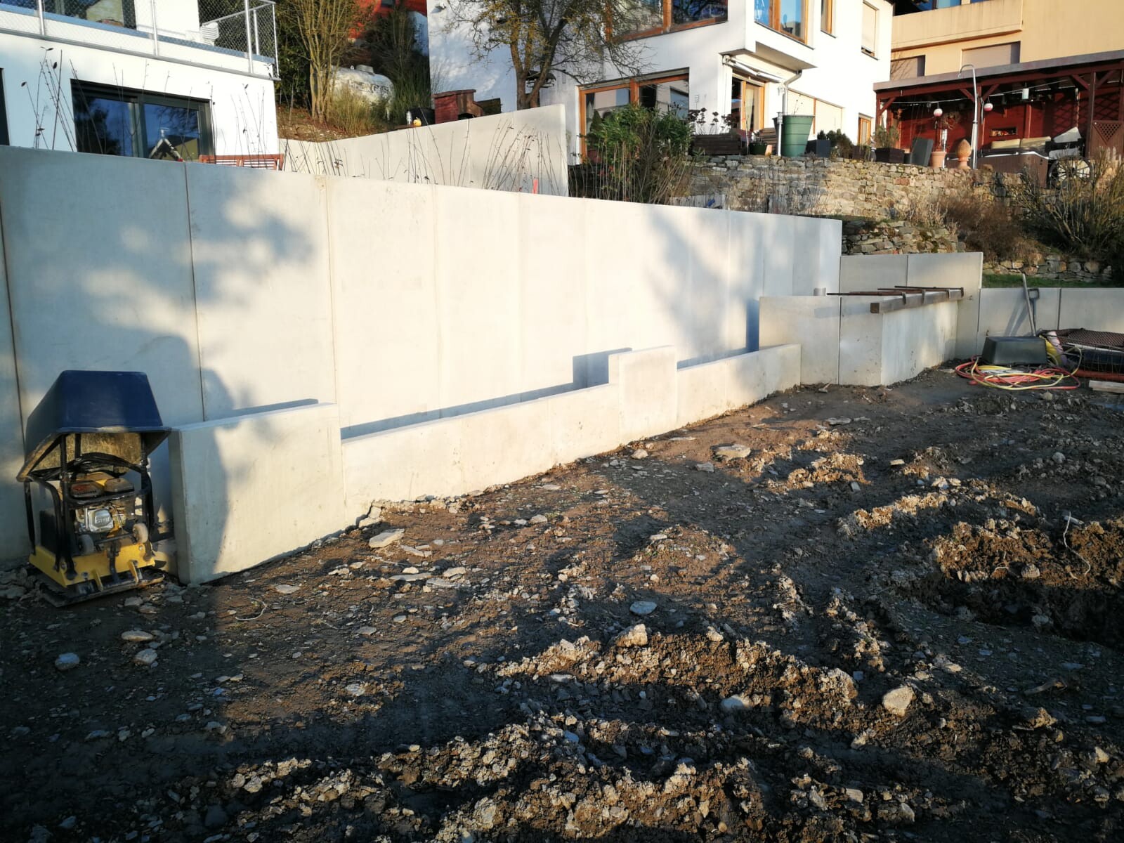 Baustelle mit hellgrauen Betonwänden, Erdreich und Bauwerkzeugen am Rand.