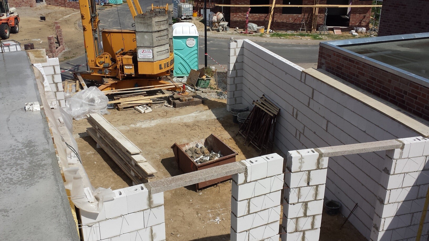 Baustelle mit weißen Betonblöcken, Baufundamenten, Holzplanken und Kran im Hintergrund