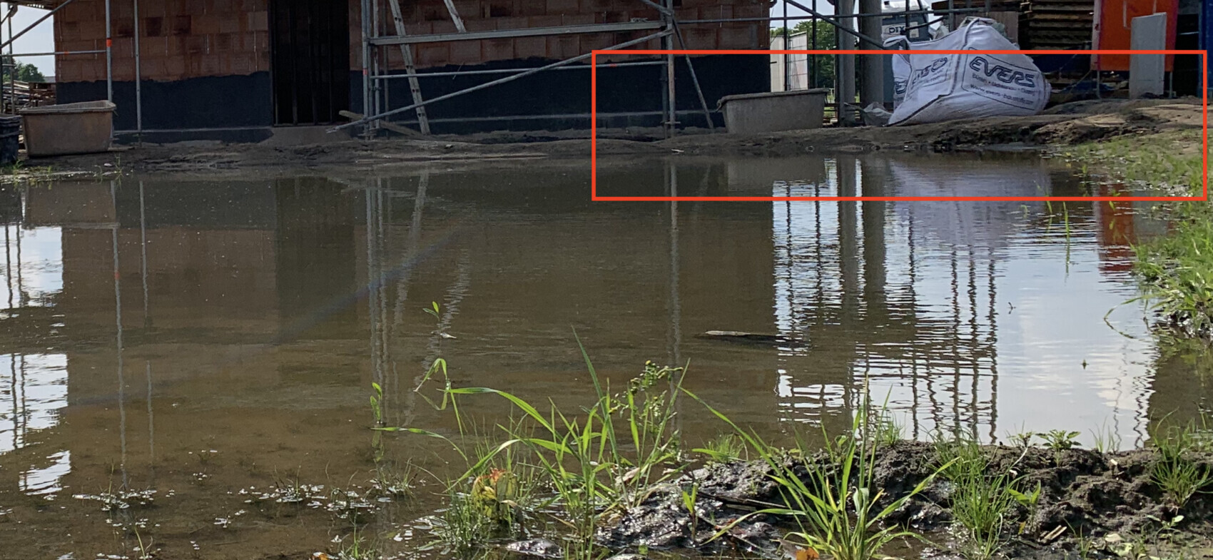 Baustelle mit Rohbau, Gerüst, stehendes Wasser und Baufundament.