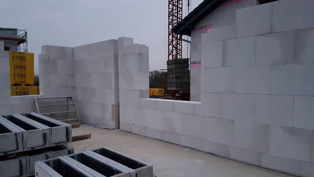 Eine Baustelle mit weißen YTONG-Steinen, halbfertige Mauer, Kran im Hintergrund.