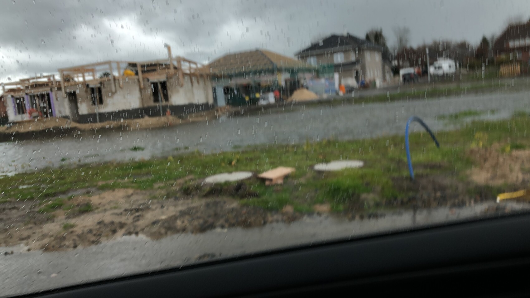 Rohbau-Bauplatz mit Holzkonstruktion, regnerischer Himmel, Grasfläche und Wasserkanal im Vordergrund