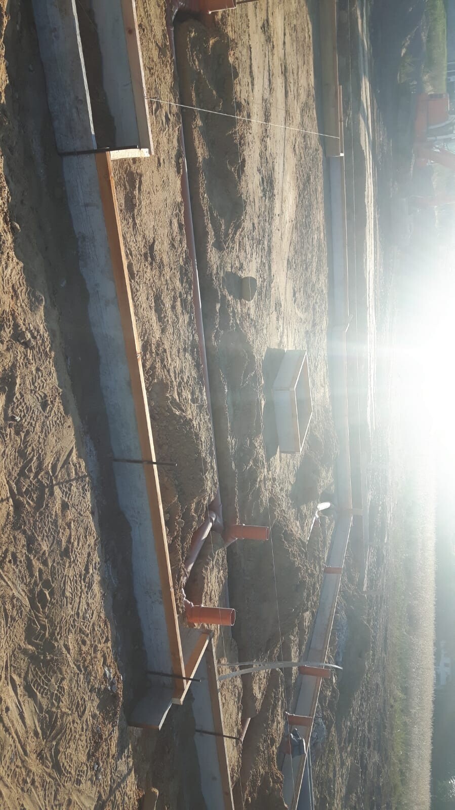 Baustelle mit Fundamentformen, Holzschalungen, Rohren und Erdarbeiten bei Sonnenlicht