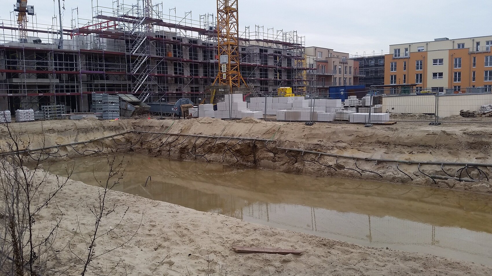 Baustelle mit Gerüst, Kran und Wassergraben vor Rohbaugebäuden