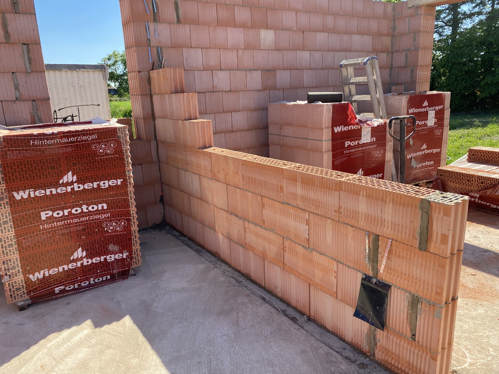 Unfertige Baustelle mit Poroton-Hintermauerziegel-Wand und gestapelten Wienerberger-Säcken.