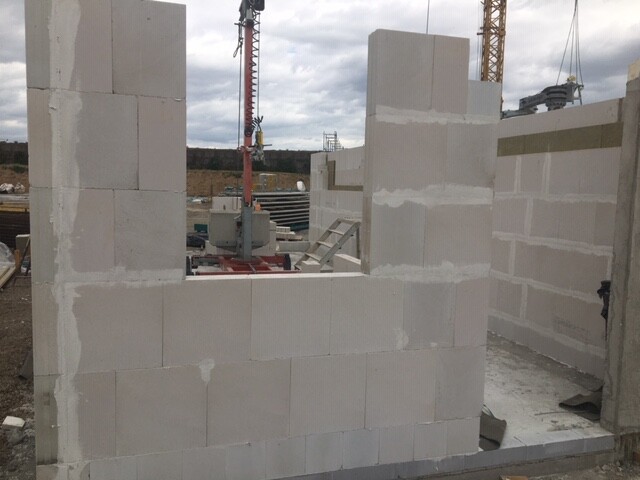Unfertige Baustellenwand aus Betonblöcken mit Baukran im Hintergrund.