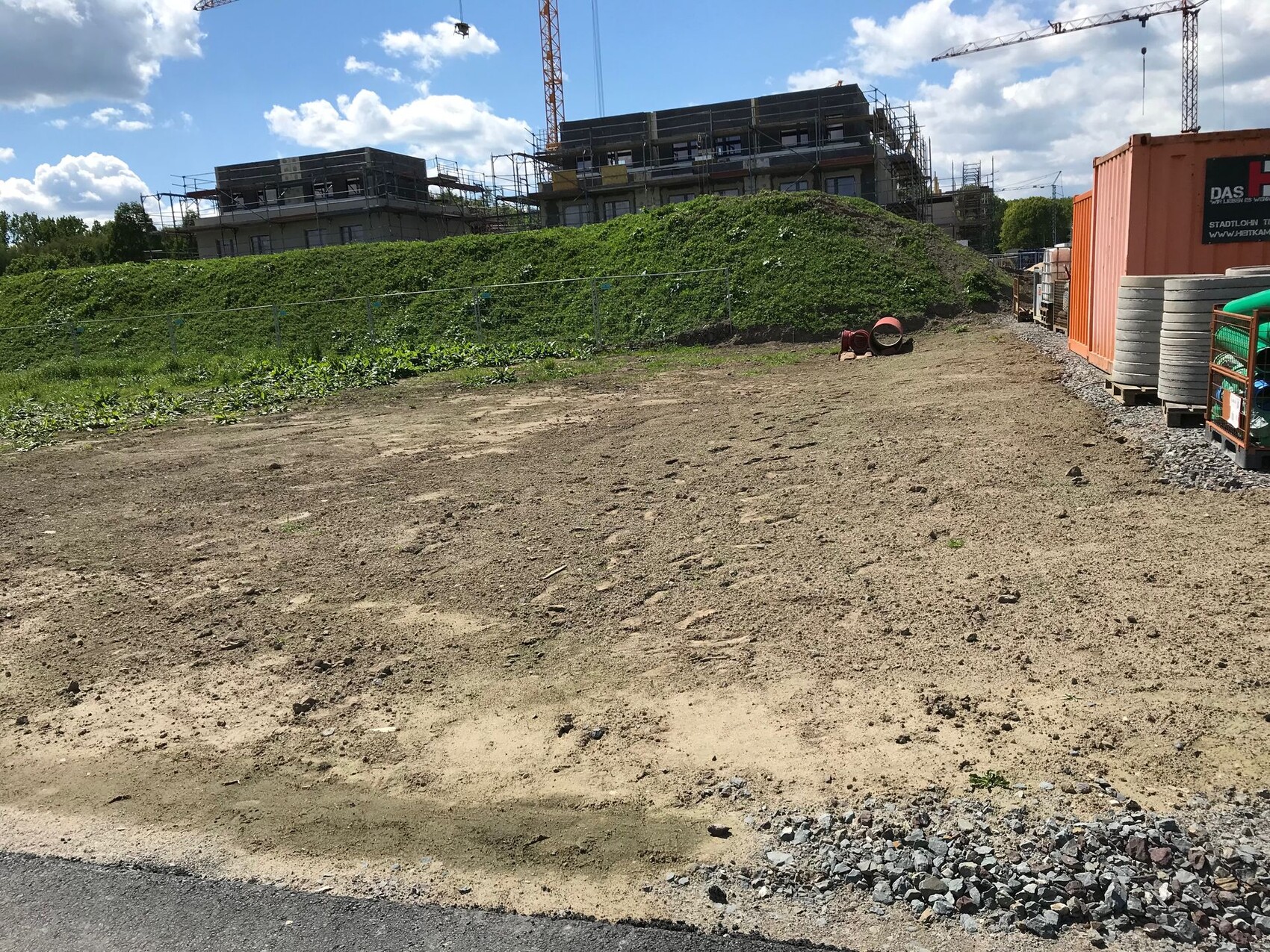 Baustelle mit unbefestigtem Boden, Gerüsten, Kranen, Baucontainern und Bauzubehör.