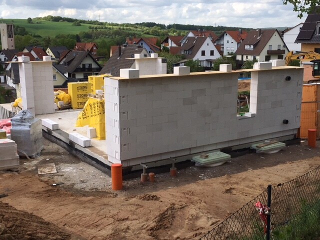 Baustelle mit weißer YTONG-Wand, gelben Dämmstoffen und Häusern im Hintergrund.