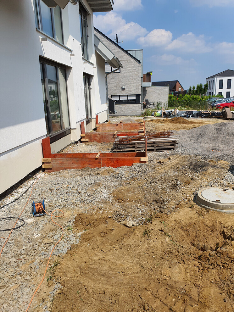 Außenansicht eines Neubauprojekts mit Erdarbeiten, Holzfundamentformen und Baugeräten
