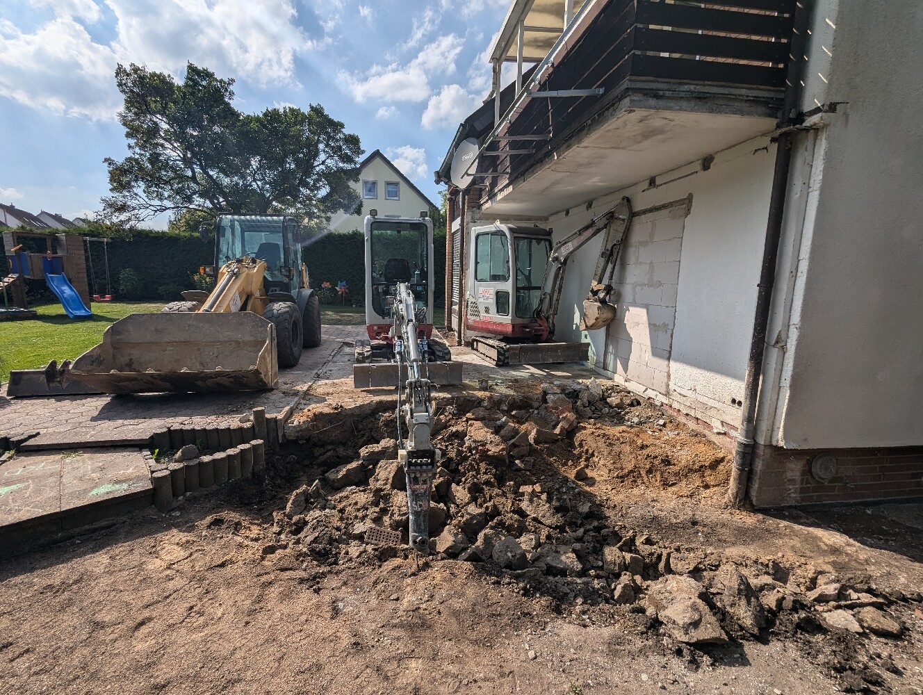 Baustelle vor Haus: Bagger arbeiten, Erde und Baugeröll vor dem Gebäude.