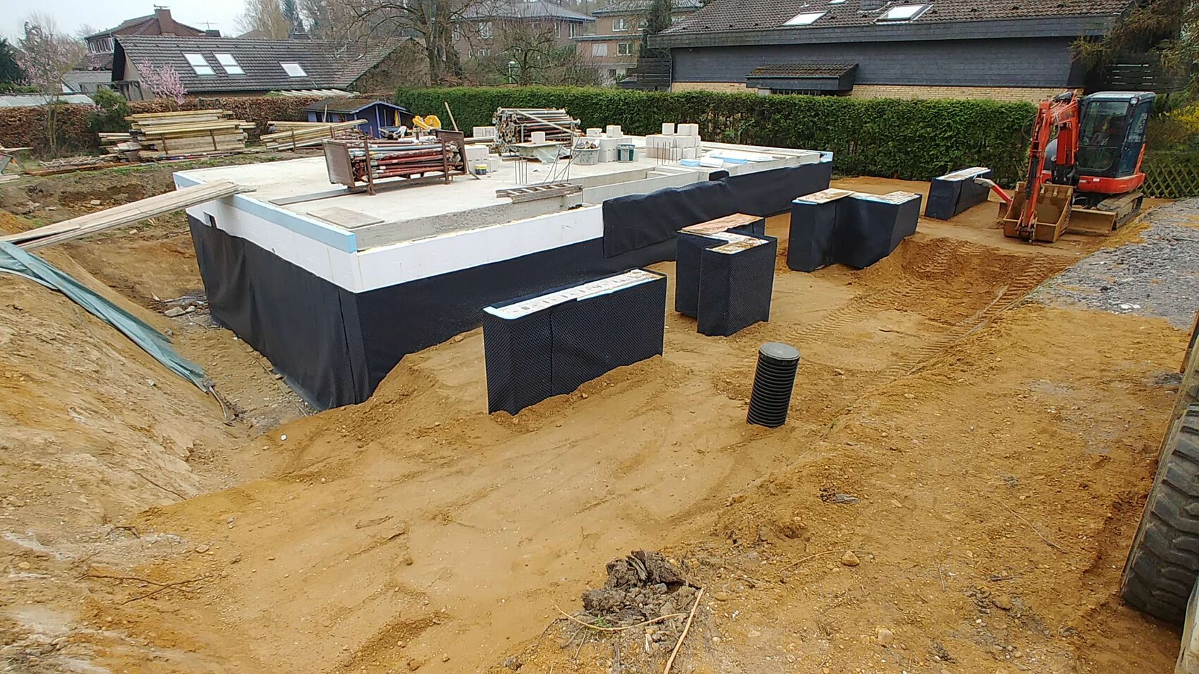 Fundament eines Wohnhaus-Bauprojekts: Dämmung, Abdichtung, Bauplatten, Baugeräte und Bagger