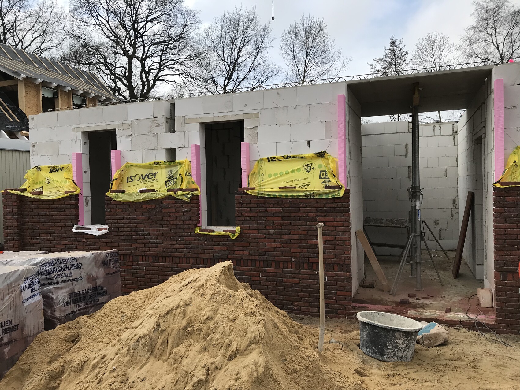 Baustelle mit Rohbau: weiße Betonblöcke, rote Ziegel, Sandhaufen und Baugerüst.