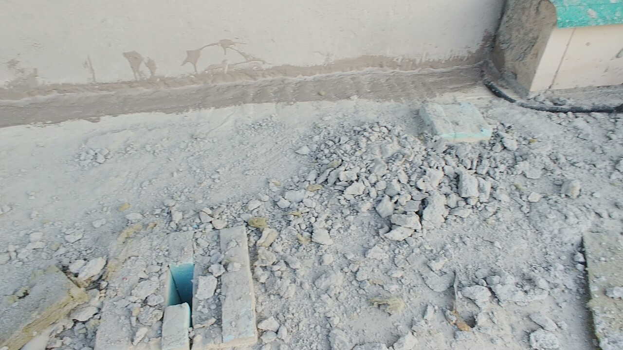 Baustelle mit Schutt, Kies und unfertigem Fundament entlang einer Wand.