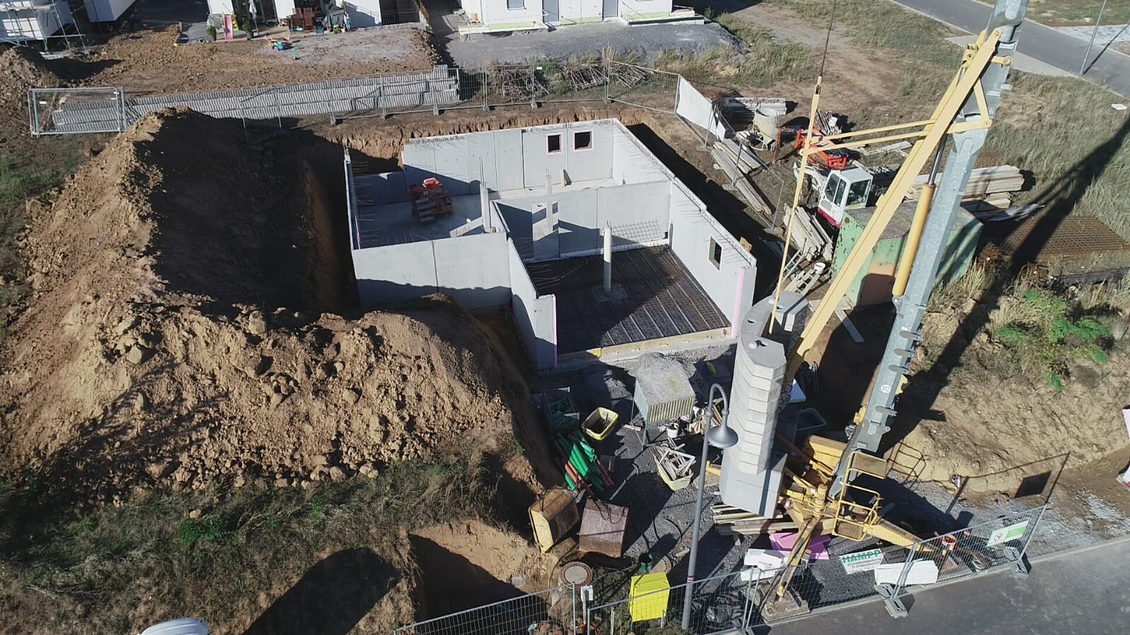 Luftaufnahme einer Baugrube mit Rohbau-Fundamenten, Betonwänden und Kran