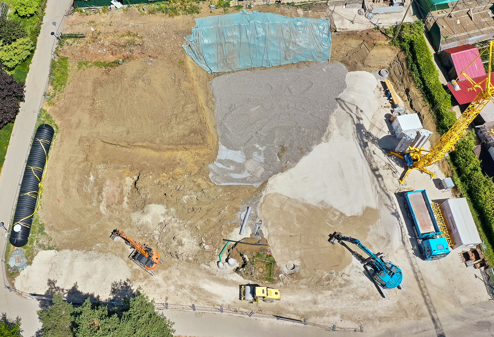 Luftaufnahme einer Baustelle mit großem Schotterhaufen, Bagger, Kran, LKW und Baumaschinen