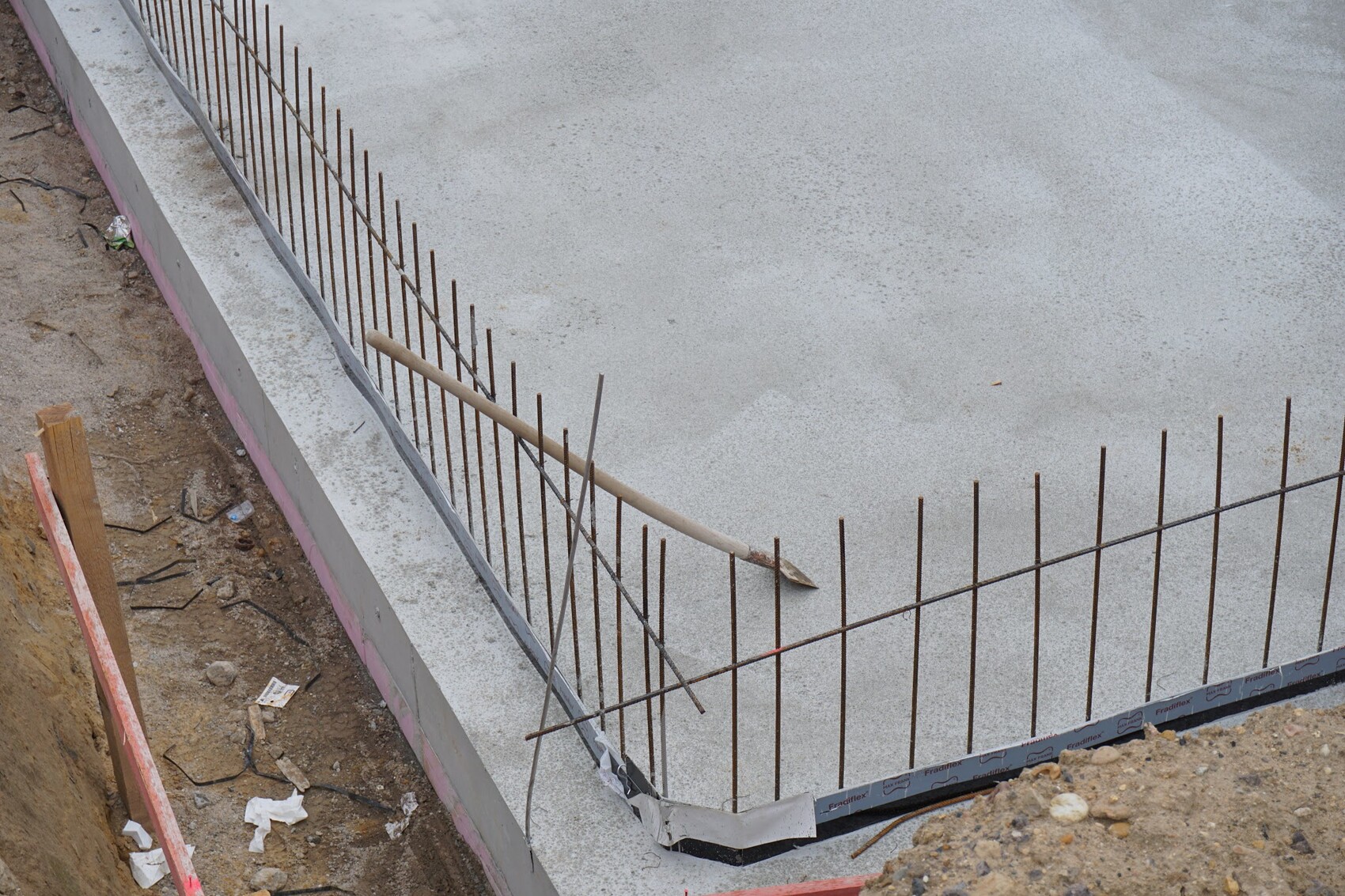 Rohbaufundament mit Bewehrungsstahl auf Baustelle und Erdarbeiten neben der Betonplatte